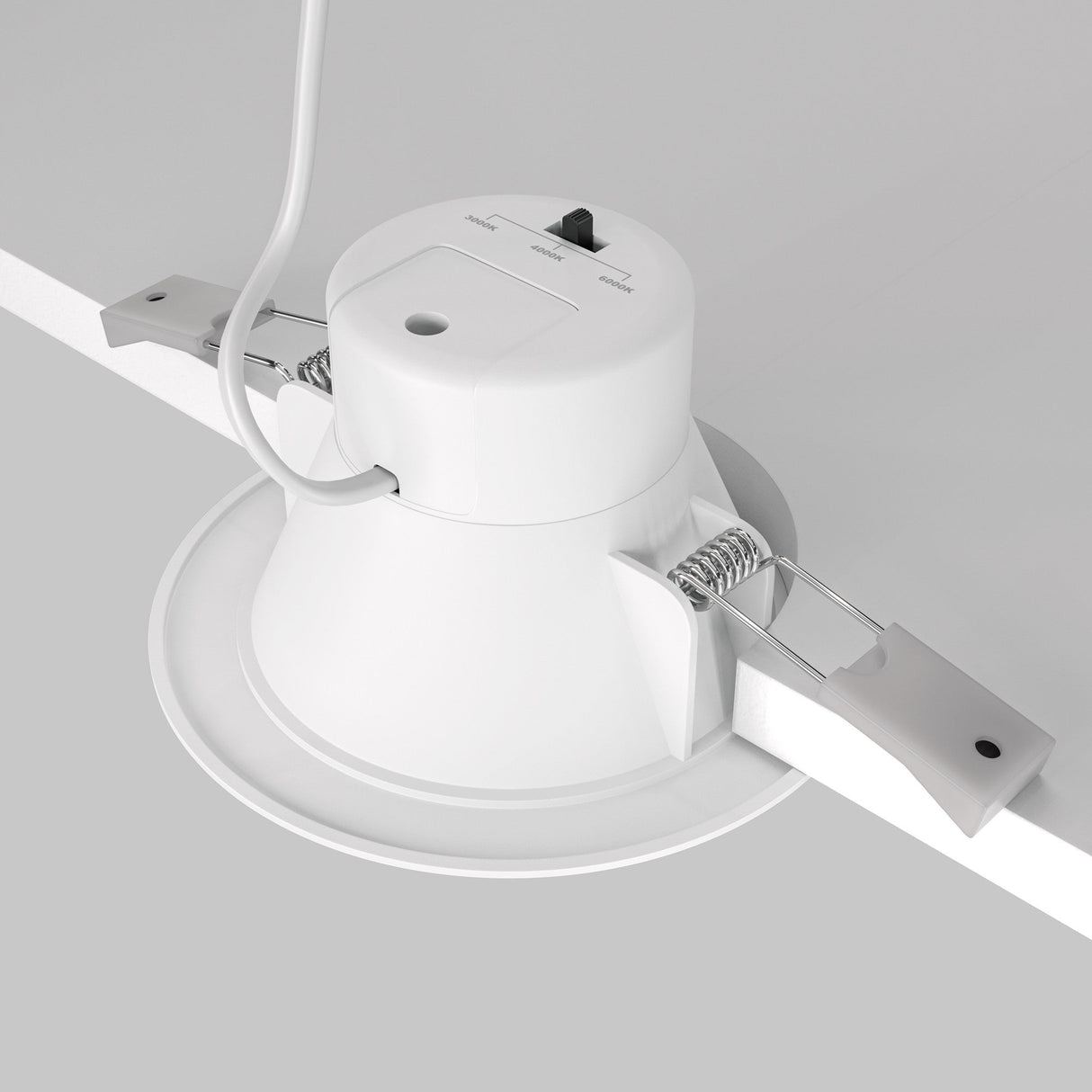 A Stockton CCT LED Round Recessed Downlight 7W 3000-6000K - White, featuring adjustable metal brackets and attached wiring, is positioned on a gray surface. Its shown from a low angle, emphasizing its round shape, installation mechanism, and energy efficiency.