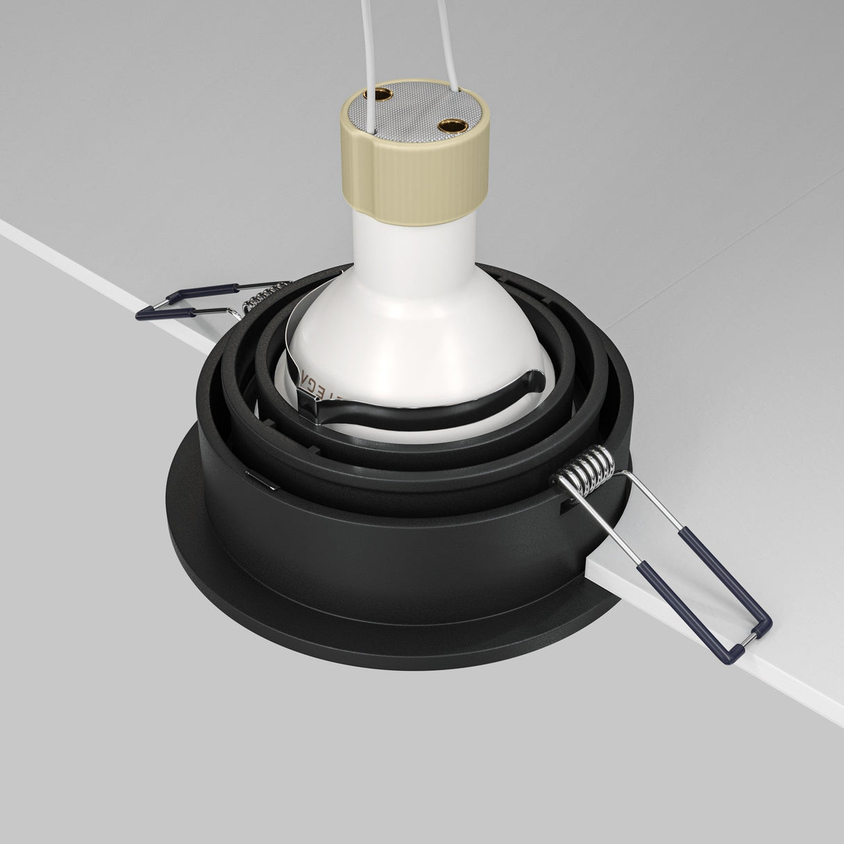 A close-up shows the Atom Single Tilt Round Recessed Downlight - Black being installed in a ceiling. This modern fixture features a white bulb holder, black circular base, and metal spring clips for secure ceiling mounting.
