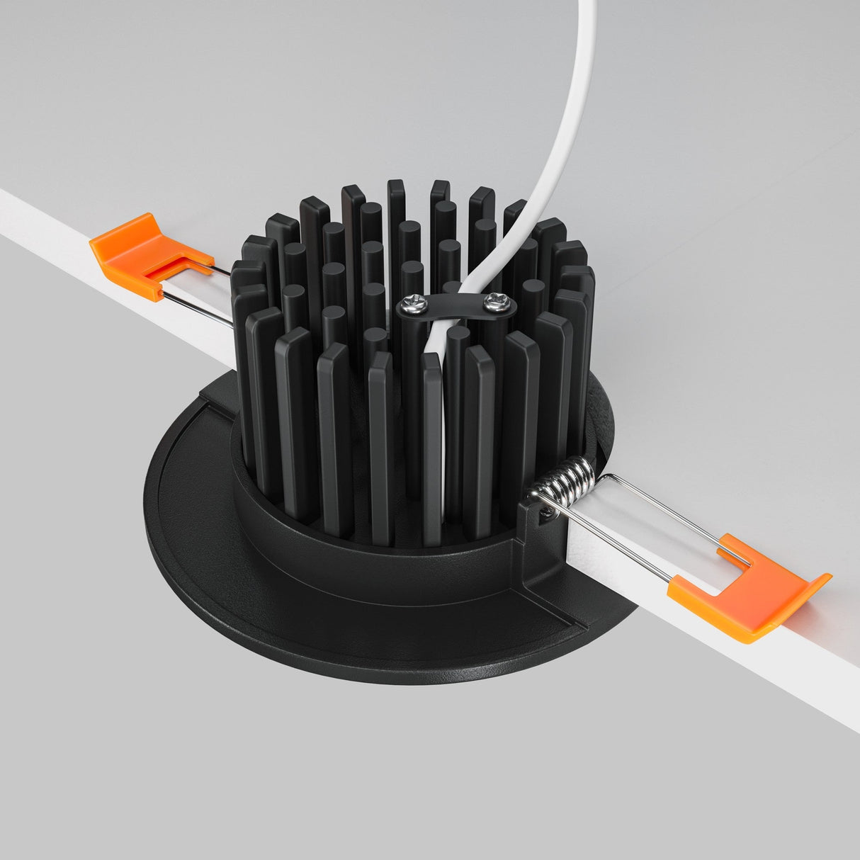A close-up shows a black cylindrical heatsink with vertical fins attached to a white panel, part of the Zen LED Round Recessed Downlight 7W 4000K. Secured with orange clips and featuring a top cable, this setup suggests an energy-efficient lighting solution.