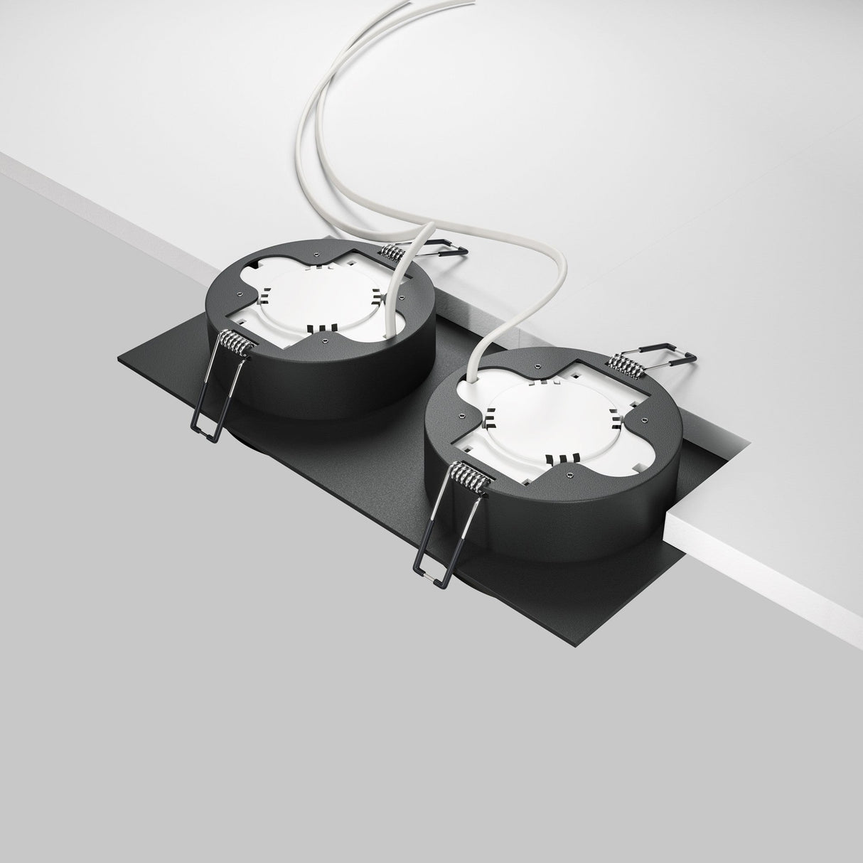 The Hoop Twin Fixed Rectangular Recessed Downlight - Black includes two circular fixtures with a sleek black finish and white interiors. Installed in a rectangular cutout, they are secured with metal clips, displaying wires against a minimalistic neutral background.