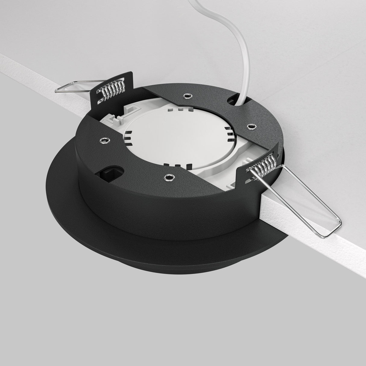 The Hoop Single Fixed Round Recessed Downlight - Black is being installed. It has a circular shape with a black outer ring, exposed spring clips, and a white interior. It features an energy-efficient LED bulb and connects via a white wire for seamless integration into modern minimalist spaces.