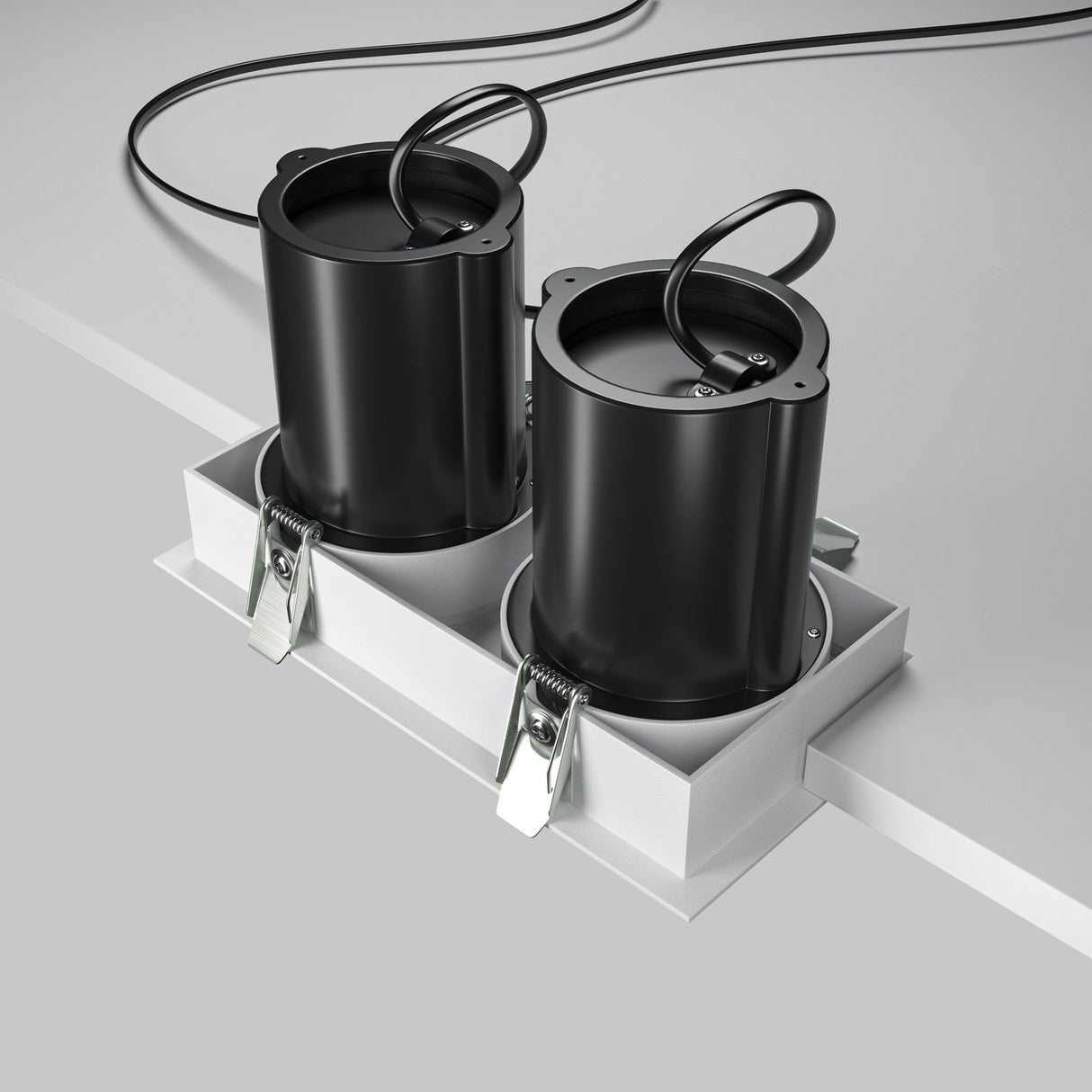 Two black cylindrical containers with attached lids and cables sit side by side on a white surface, secured in a tray with metallic clips. They resemble the sleek Hidden Twin Adjustable Retractable In-Out LED Rectangular Recessed Downlight - White, known for its high CRI rating.