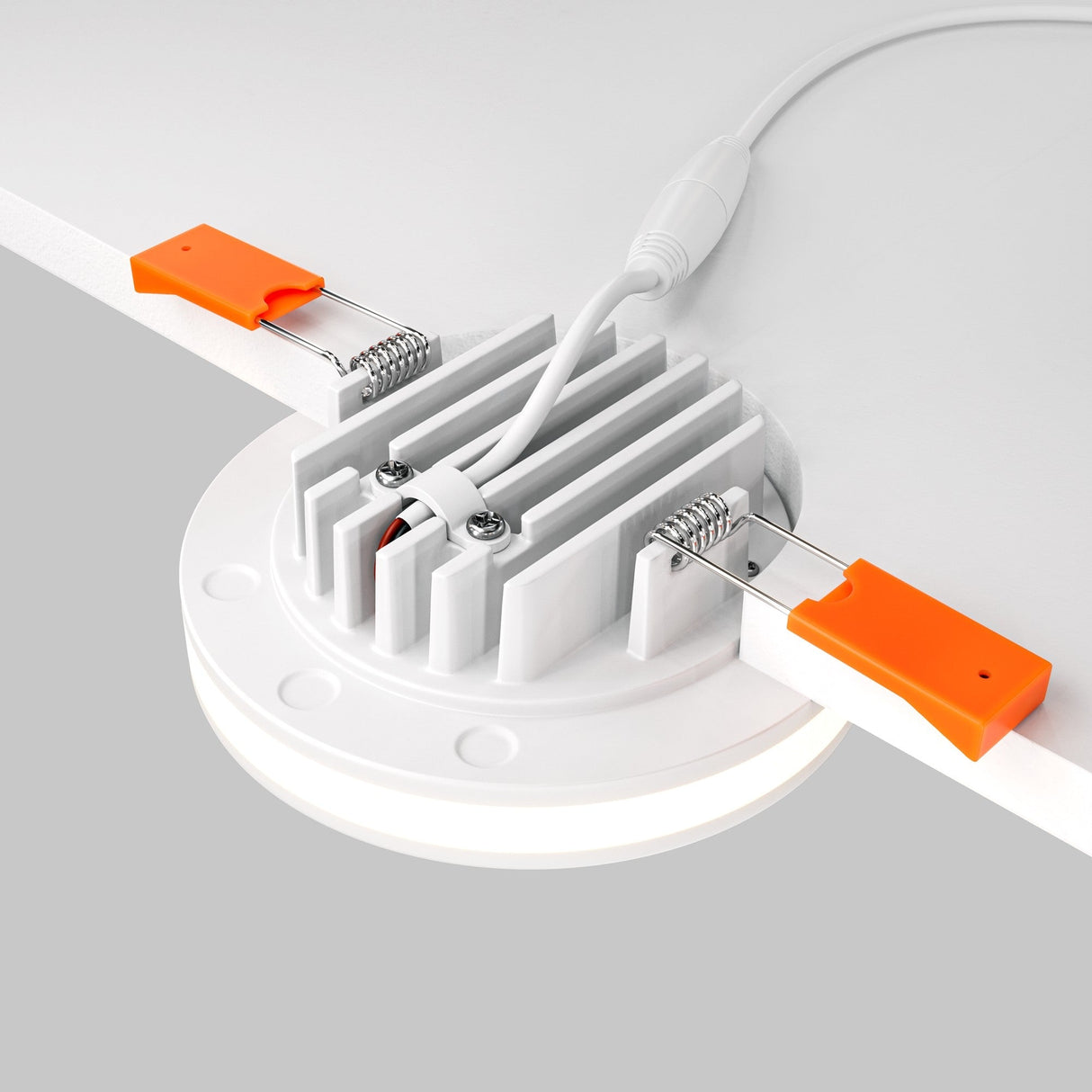 The Phanton LED Recessed Downlight 12W 3000K, featuring a round design with a white base and cooling fins, is installed on a white ceiling. It includes bright orange spring clips for easy setup, provides 3000K illumination, and offers wide light dispersion with its connected power cable.