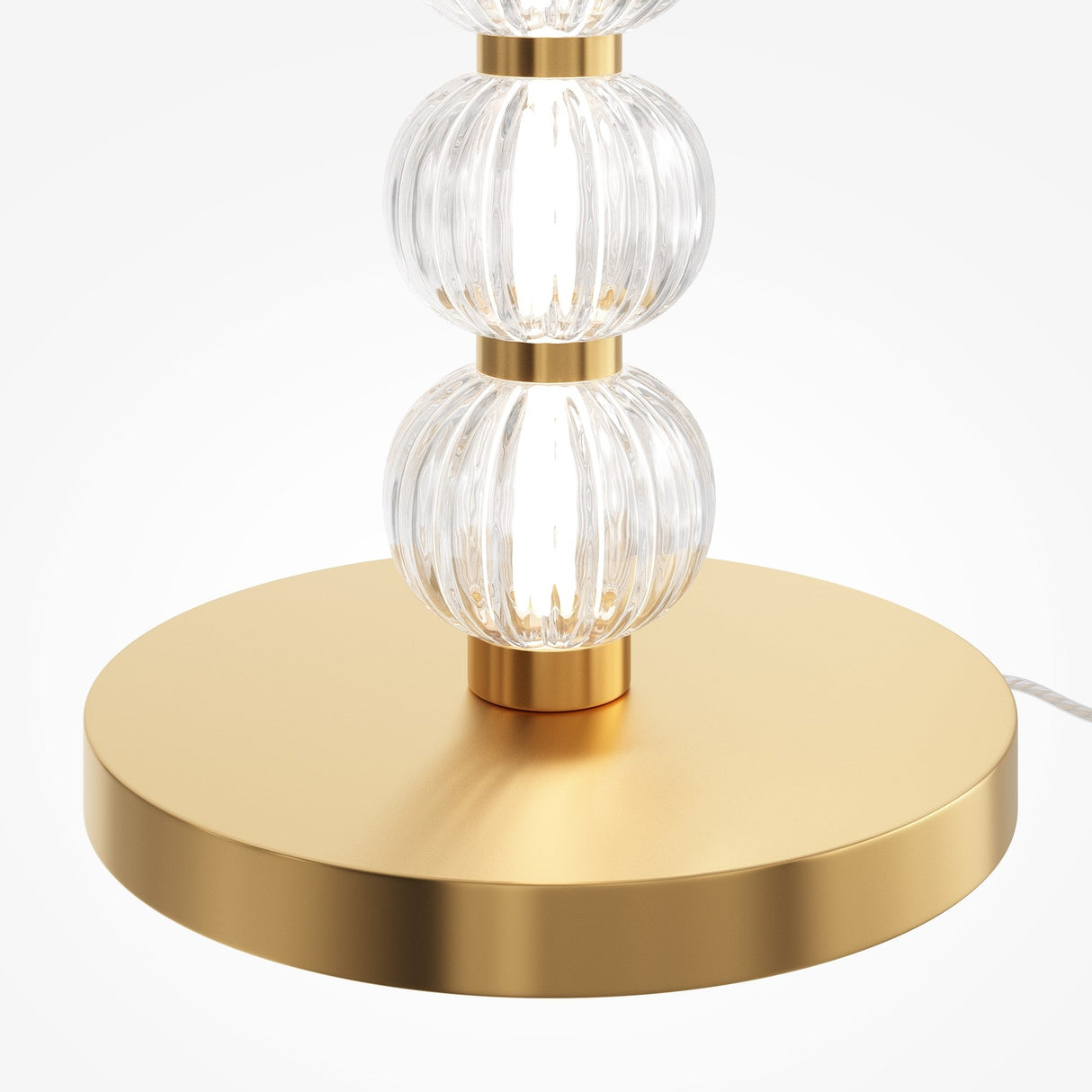The Amulet LED Floor Lamp - Gold features three stacked ribbed glass spheres on a round gold-finish base. These textured spheres reflect light elegantly, offering a stylish look, while the cord discreetly extends from the base to maintain design flow.