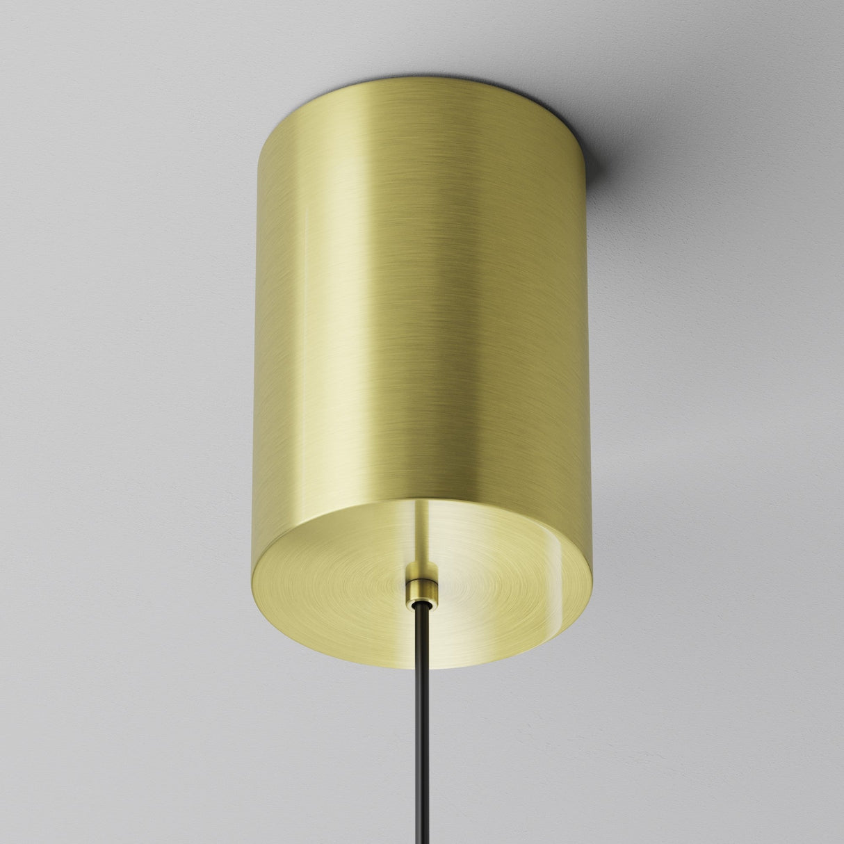The Plato LED Pendant Light - Brass features a modern design with a cylindrical brass shade, suspended from a black cord against a white ceiling.
