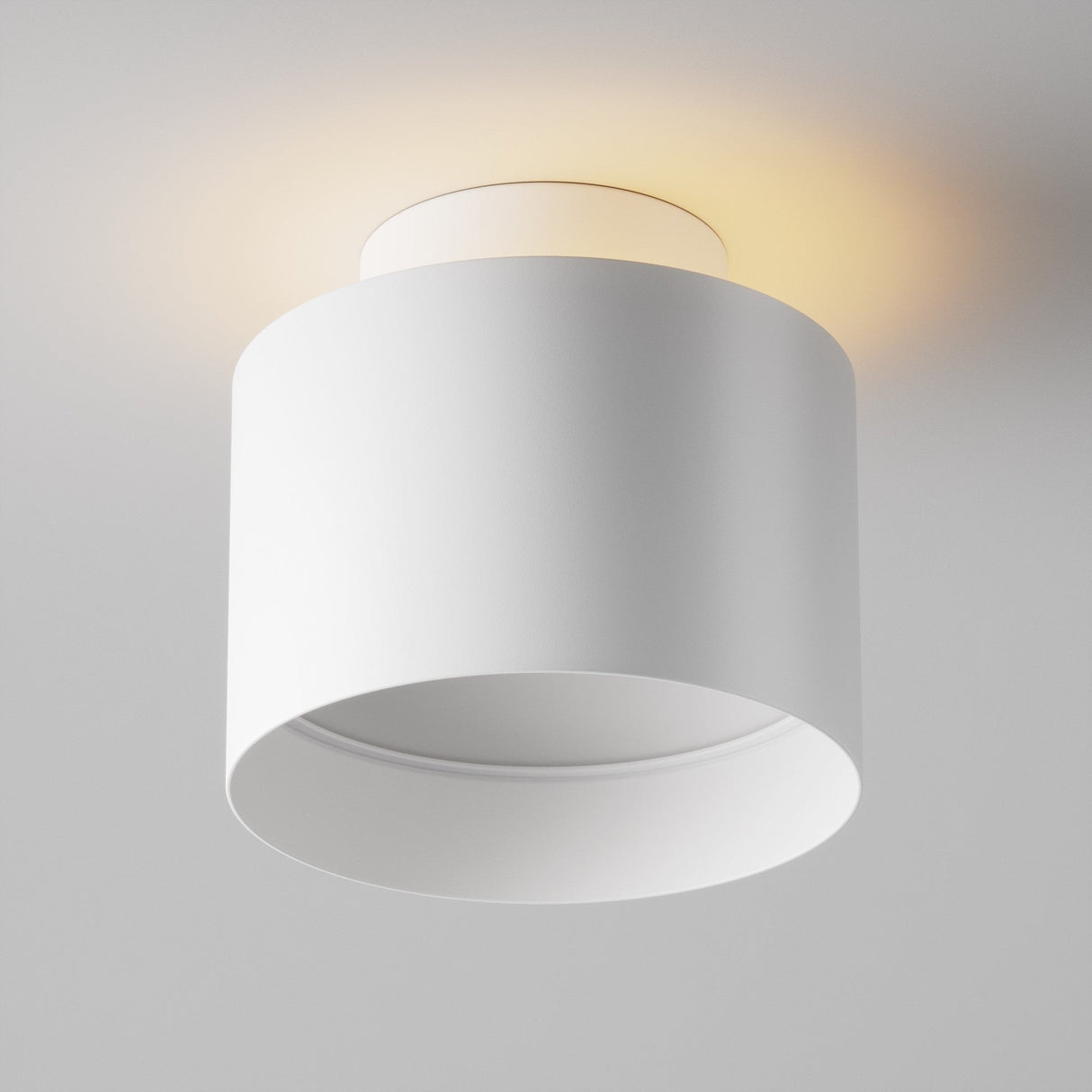 The Planet LED Small Round Surface Downlight 3000K - White is a minimalist cylindrical ceiling fixture, casting a warm glow against the light gray background and exemplifying energy-efficient lighting.