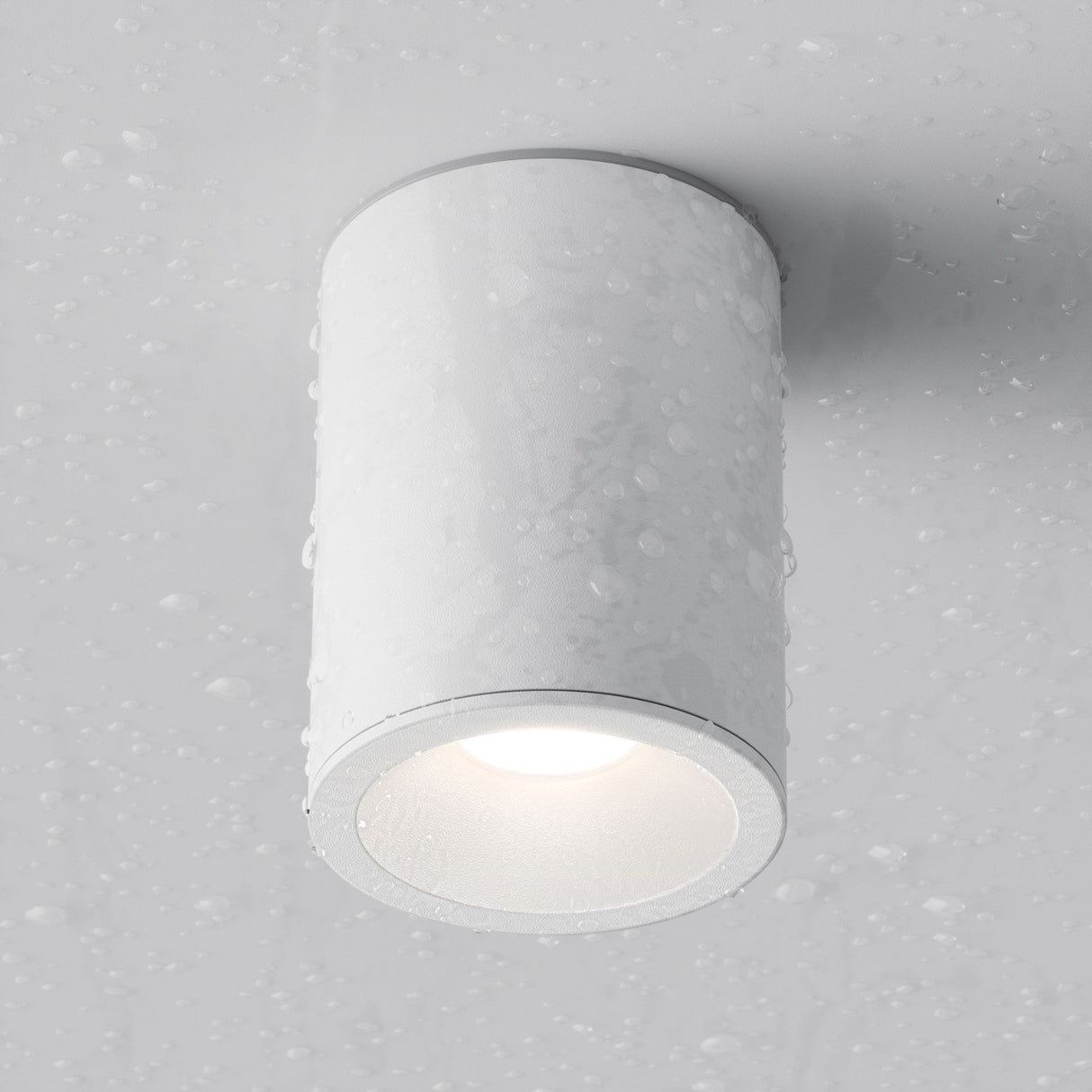 The Zoom Round Surface Downlight - White is a cylindrical modern ceiling light with an aluminum body, IP65 protection, and a sleek design. Positioned against a grey background and covered in water droplets, its ideal for wet environments and adds functionality to any space.