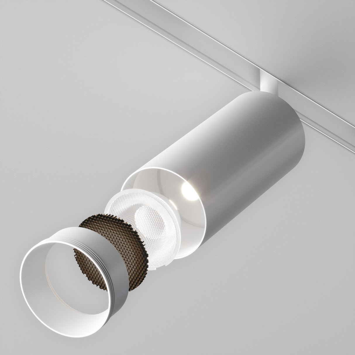 A Focus LED Medium Decorative Ring for Track Spotlight in white is ceiling-mounted, part of an advanced system. Its front cover is partially disassembled, showing internal components like a light bulb and perforated structure, set against a light gray background.