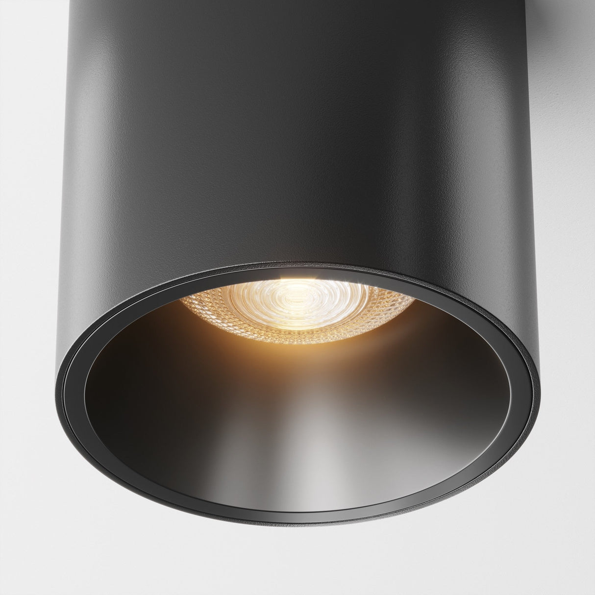 Close-up of the Alfa LED Dimmable Fixed Round Surface Downlight 12W 3000K - Black, featuring a modern cylindrical design and illuminated bulb. This industrial downlight emits a warm glow, highlighting its sleek design and smooth surface.