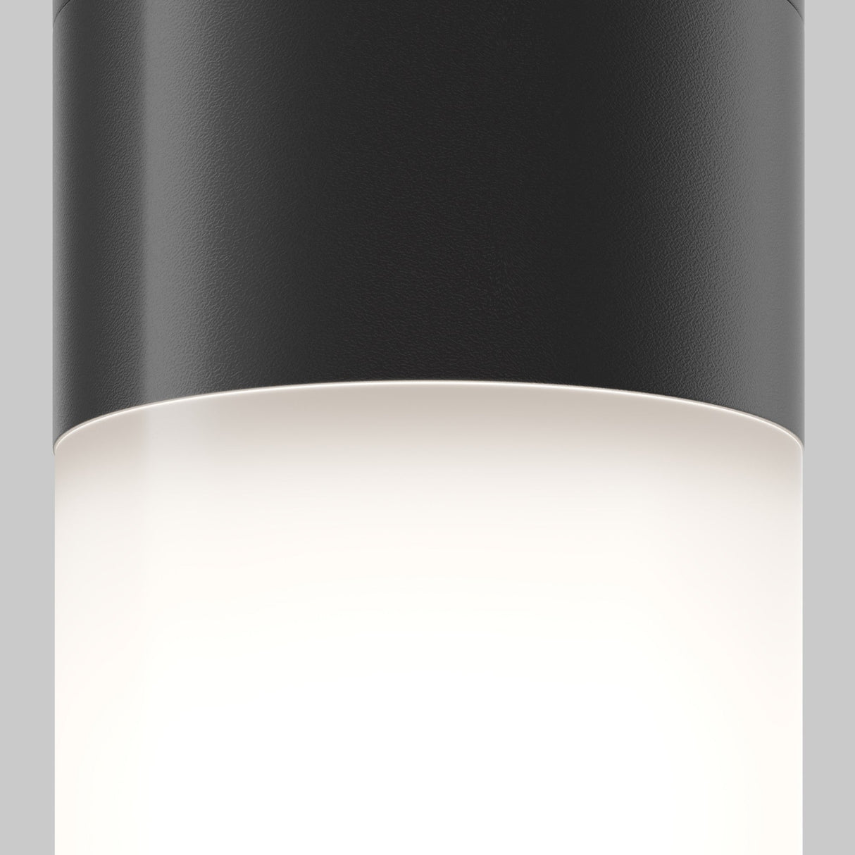A close-up of the Willis Outdoor Downlight - Black, a modern cylindrical ceiling fixture with a black matte finish and glowing white diffuser, crafted from durable metal for even illumination. Ideal for exterior spaces against a plain light gray background.
