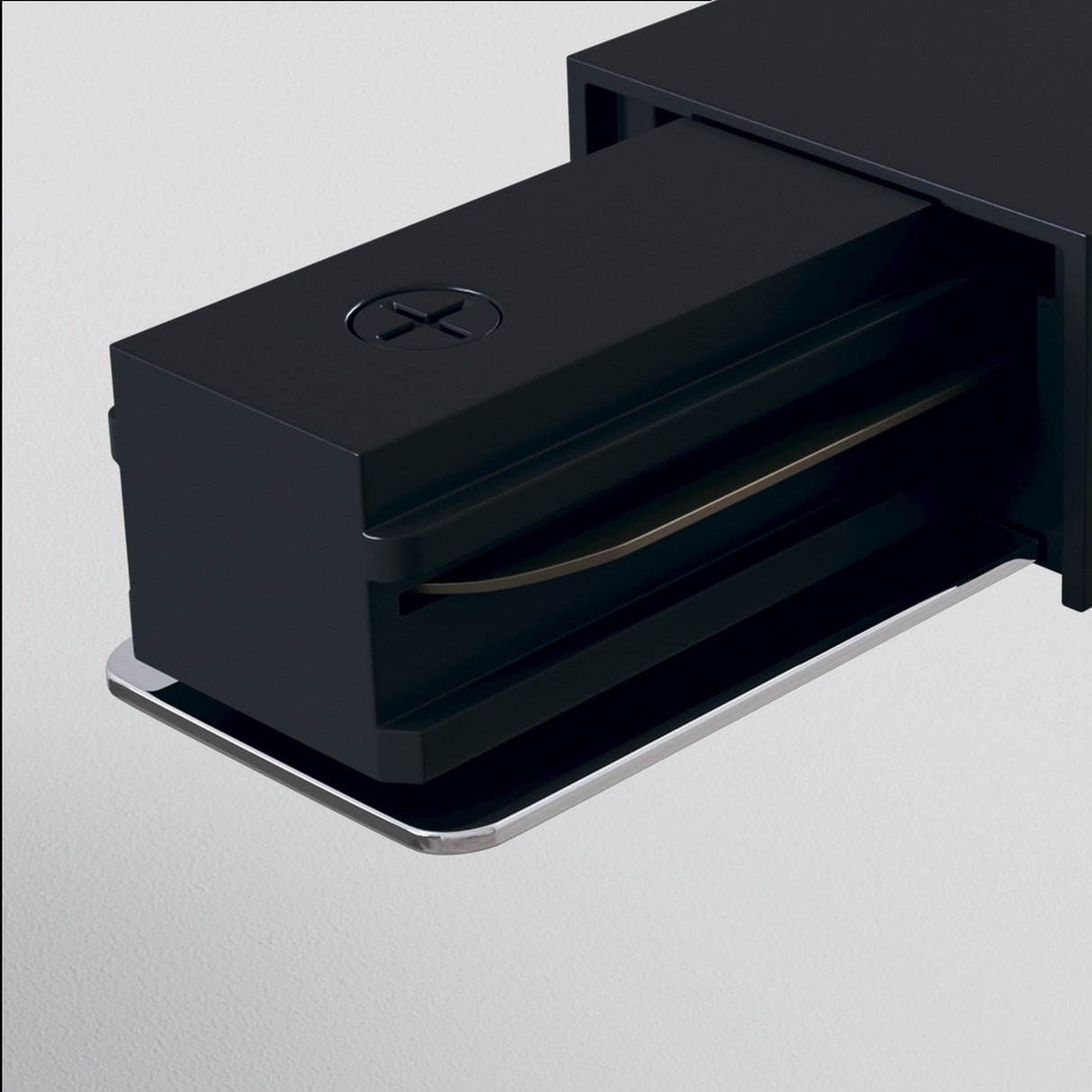 The Unity Single Phase Track Power Feed - Black is a modern, sleek wall-mounted handle with a rectangular design and subtle metallic accents. It resembles black track systems and features a cross-shaped indentation on top, all set against a light gray background.