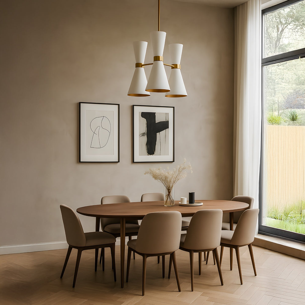 A modern dining room features a wooden oval table, six beige chairs, abstract art on the beige wall, tall curtains, a large window with a garden view, and the Ramses 3 Light Chandelier - White overhead. Dried flowers in a vase decorate the table.