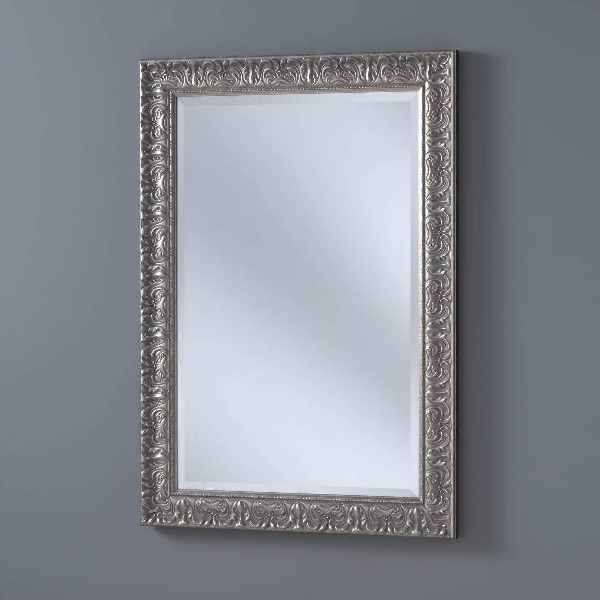The Elyssar Rectangle Wall Mirror in silver features an ornate frame with intricate floral and swirl designs. Its elegant style complements a plain gray background, enhancing any space with subtle light reflection and sophistication.