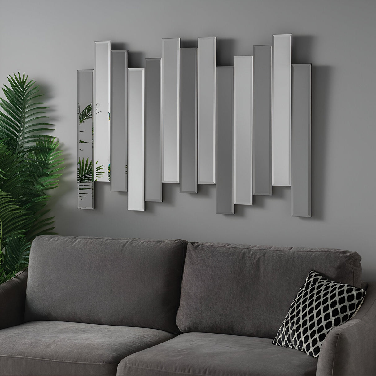 The Levira Panel Wall Mirror - Grey showcases a geometric design with vertical mirrored panels, adding modern sophistication above a gray sofa accented by a black and white patterned pillow. Nearby, a green plant introduces an element of nature into the contemporary living space.