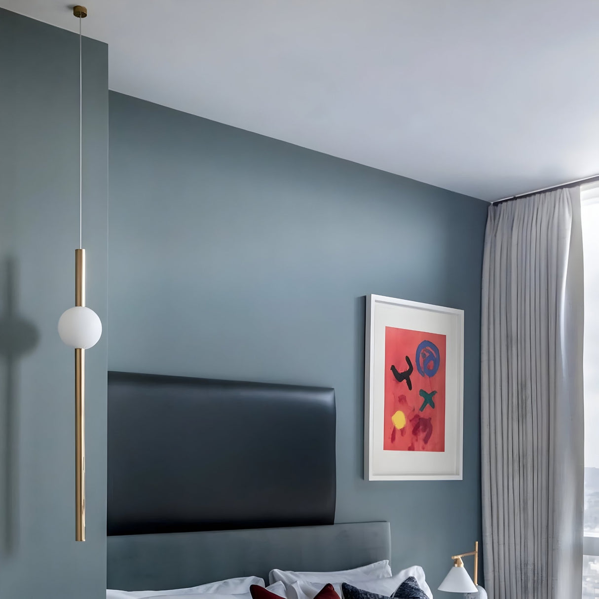 A modern bedroom with muted blue walls, a black headboard, white curtains, and abstract art above the bed features a minimalist design highlighted by the Sottile LED Vertical Suspension Light in gold for an elegant touch.