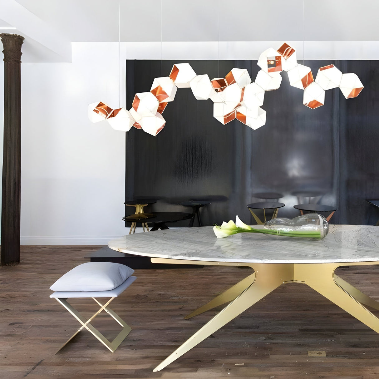 Modern dining area with a round marble table, gold base, and cushioned bench. The Spar Linear Suspension Light in white & gold hangs above, complementing dark walls, wood floors, and minimalist decor for a refined modern look.