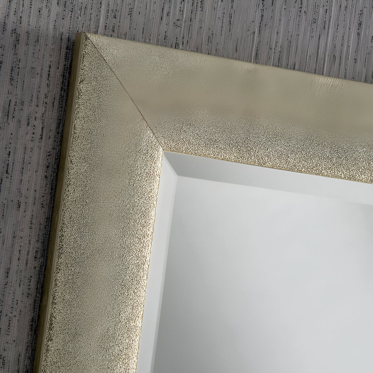 Close-up of a textured, metallic silver picture frame with a simple geometric design, evoking the Stardust Rectangle Wall Mirror - Champagne. The frame rests against a gray, vertically striped wall and encloses a blank white surface, adding an element of luxury home decor.