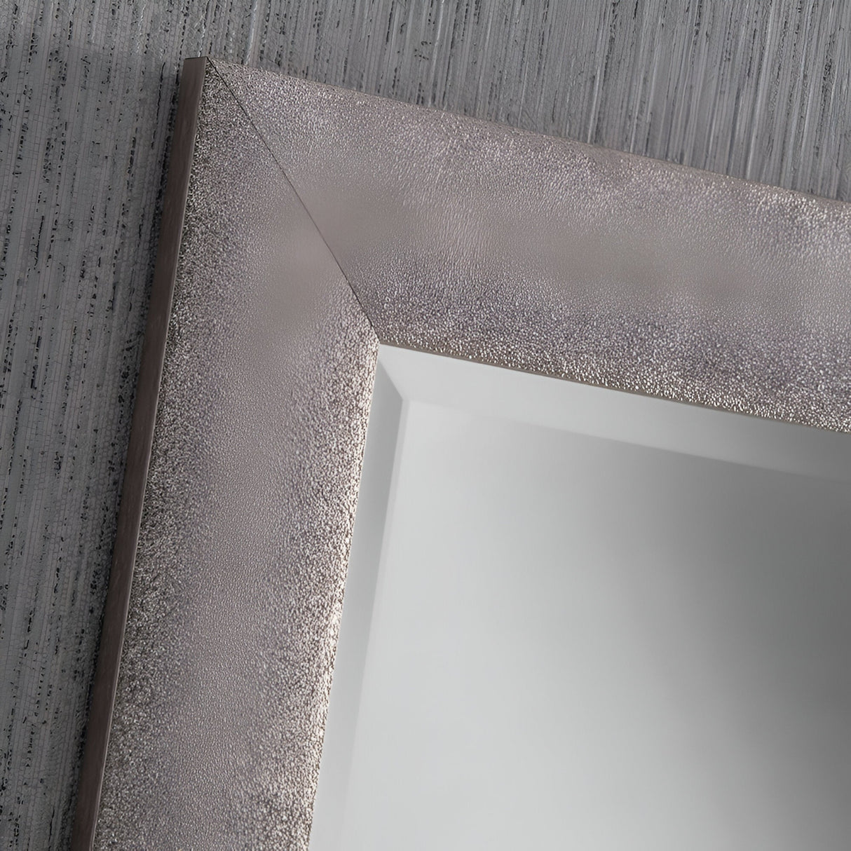 A close-up of a minimalist composition highlights the Stardust Rectangle Wall Mirror - Grey against a textured gray wall. The frame exhibits a shiny, brushed finish with distinct borders and angled joints, while its mirrored surface gently reflects light.