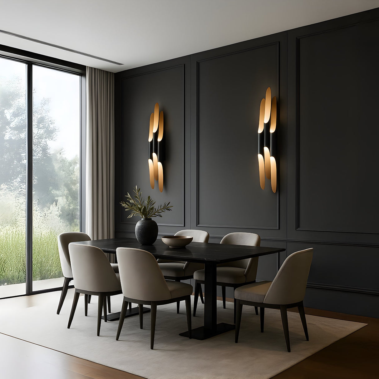 A modern dining room features a dark wood table, six beige chairs, black paneled walls, and two Stealth 6 Light Wall Lights in brass & black. A large window reveals greenery outside, while a vase and bowl decorate the table.