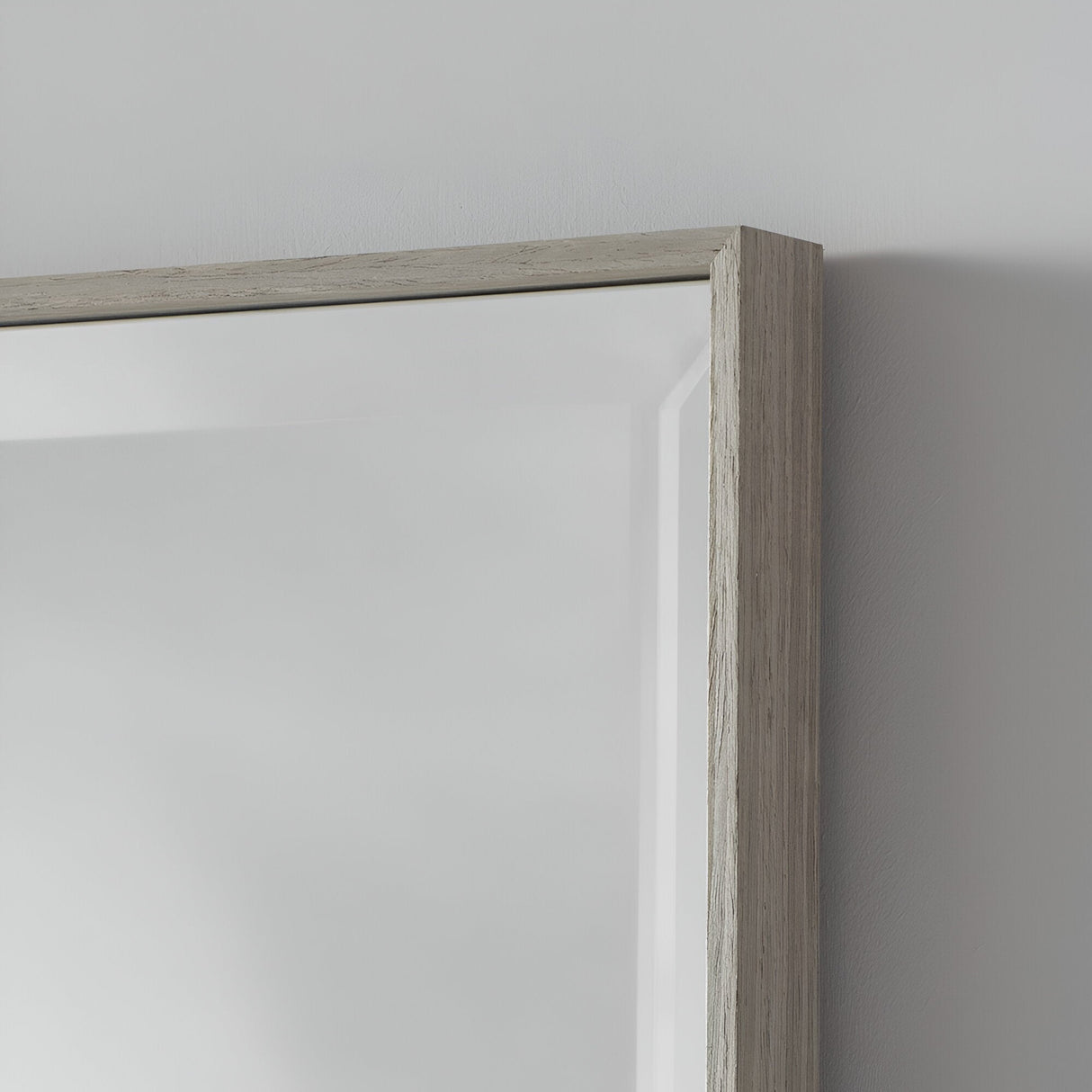 Close-up of the Aetheris Rectangle Wall Mirror in a minimalist design featuring a light wooden frame, mounted on a plain white wall. The textured frame accentuates natural wood grain patterns, while its minimal reflection showcases a soft, blurred surface that complements modern home decor.