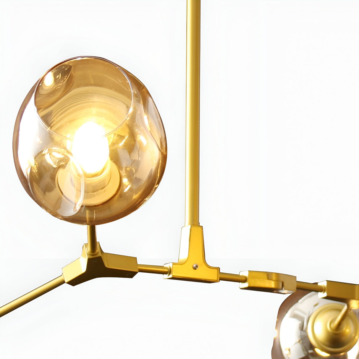 Close-up of the Niori Tree 6 Light Suspension in gold, showing an illuminated amber glass globe on a curved metal arm against a white background.