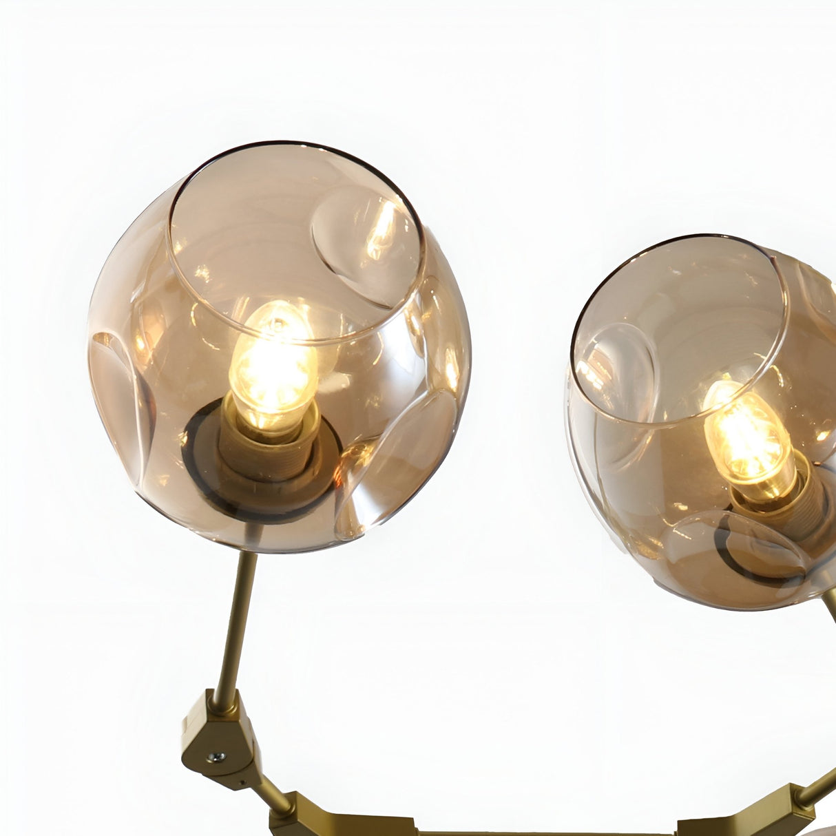Close-up of two arms of the Niori Tree 6 Light Suspension in gold, showing tinted amber glass globe shades with exposed bulbs on a white background.
