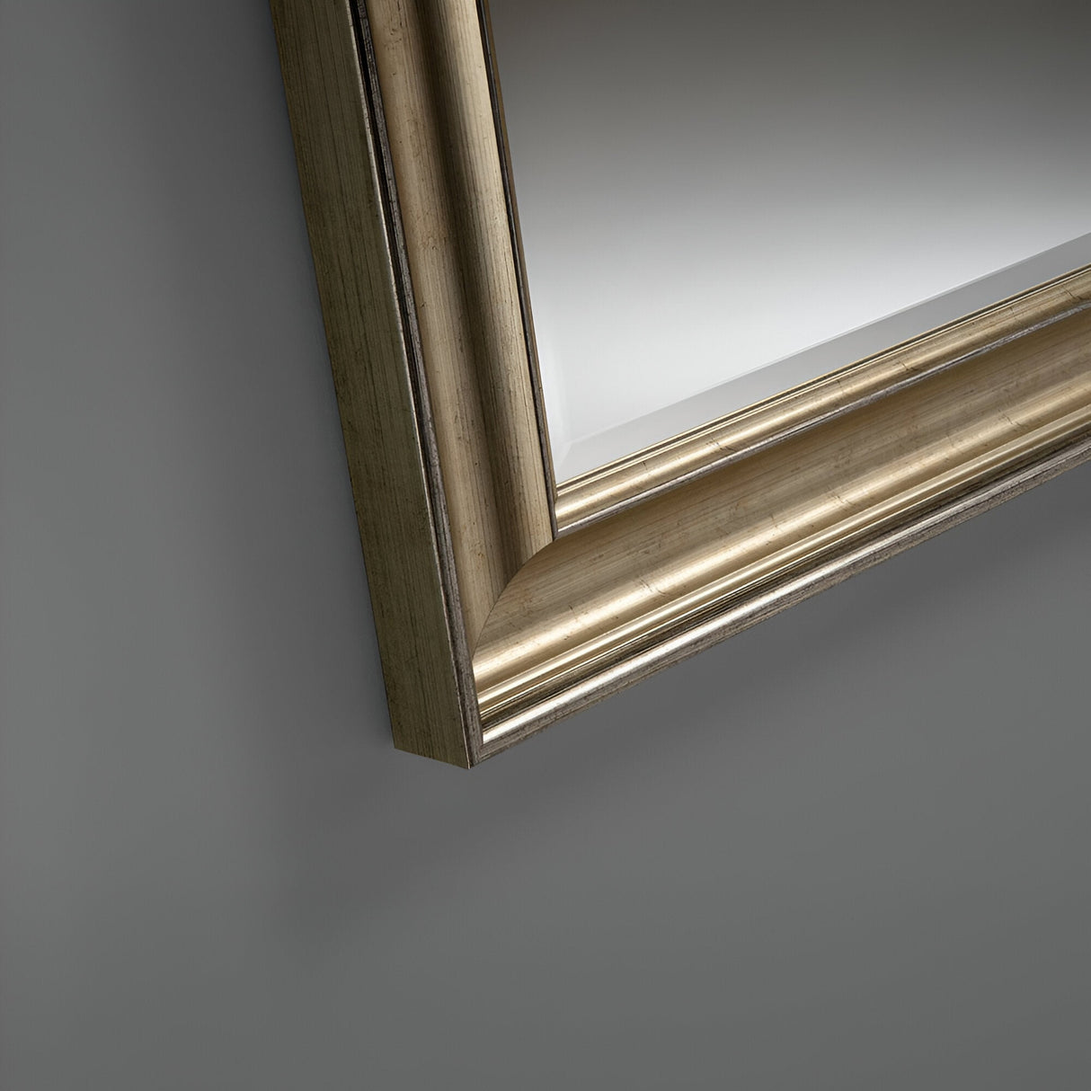 A close-up of the Luxon Rectangle Wall Mirror in Champagne highlights its elegant appeal with an ornate, gold-hued frame. The reflection transitions from a deeper gray to a lighter shade, suggesting ambient light, and the frame's texture and metallic sheen are vividly displayed.