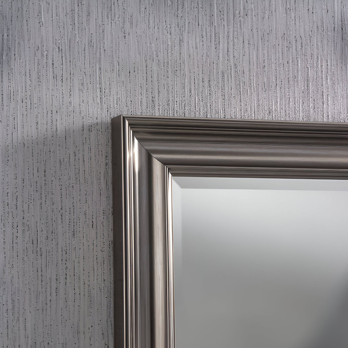 A close-up of the Luxon Rectangle Wall Mirror - Grey hangs on a wall embellished with textured, vertically-patterned wallpaper. Only a portion of the mirror and the nearby wallpaper is visible, highlighting the elegant simplicity of this home decor piece.