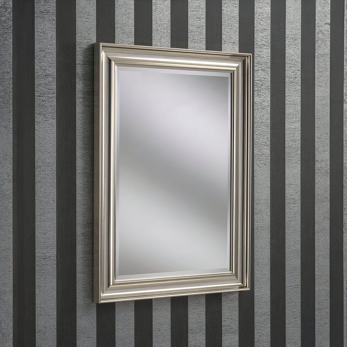 The Luxon Rectangle Wall Mirror - Silver is mounted on a wall featuring vertical black and gray stripes. Its blurred reflection captures a modern, minimalist aesthetic, making it ideal for contemporary home decor.