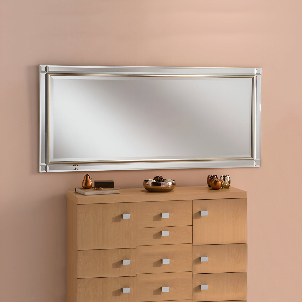 A large Lusterra Rectangle Wall Mirror - Champagne is mounted on a beige wall above a multi-drawer wooden dresser. The dresser features small sculptures and a bowl that add luxury and elegance to the room's minimalist aesthetic.
