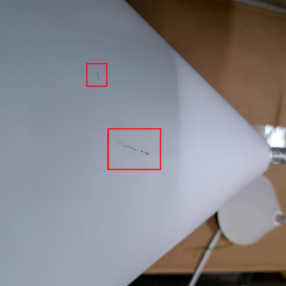 Close-up of the matte white surface of an Ex-Display Funk Stout Large Pendant Light with two small red rectangles highlighting black marks. The Scandinavian deco-style background is blurred, with a partially visible gray object on the bottom right.