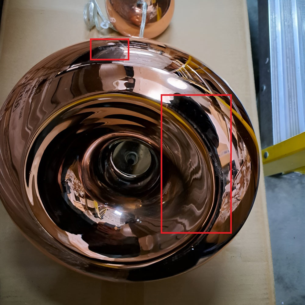 The Ex-Display Gulf Pendant Light - Copper is shown as a shiny, reflective bowl with highlighted red rectangles. Its surface captures a partial person near a shelf and exudes energy-efficient elegance while resembling an upright metallic bowl.