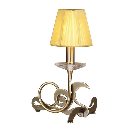 The Acanto 1 Light Table Lamp features an antique brass metal base with artistic swirls, a clear glass accent below the socket, and an amber cream shade for a decorative touch.
