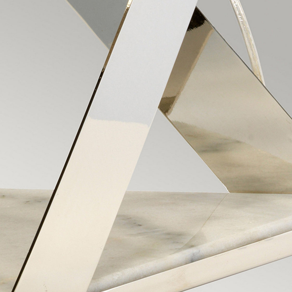 Close-up of a modern furniture piece with intersecting geometric metal frames and a reflective, polished surface. The design is complemented by the Aegeus 1 Light Table Lamp in Polished Nickel, featuring a marble base that enhances the visual appeal with its sleek presence.