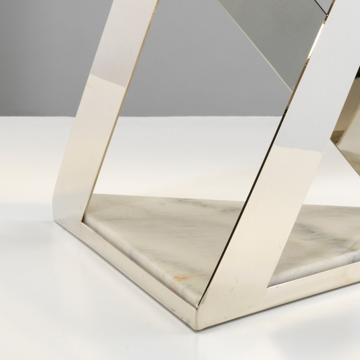 Close-up of the Aegeus 1 Light Table Lamp in Polished Nickel, showcasing sleek, intersecting metallic frames set atop a white marble base. The geometric and minimalistic design is highlighted against a neutral gray backdrop.