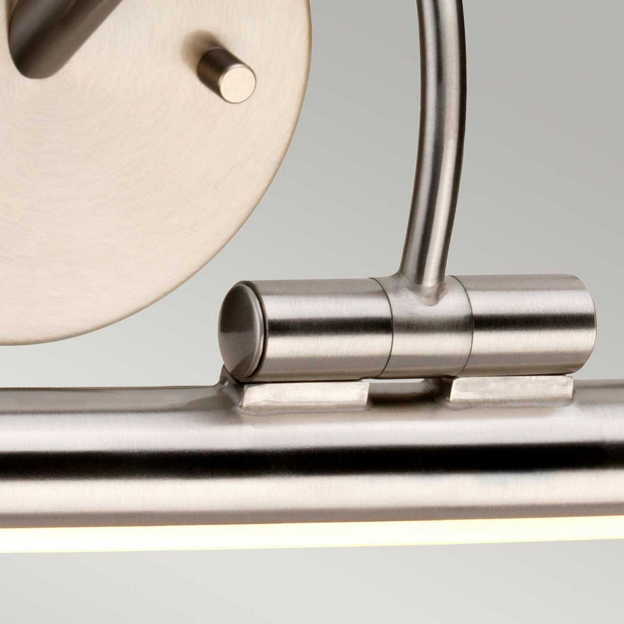 Close-up of the Alton 1 Light Small LED Picture Light - Brushed Nickel, featuring a cylindrical design. The brushed nickel surface is smooth and polished, with a thin rod attaching the fixture to the wall mount. Perfect for art lighting or as an LED picture light to enhance any space.