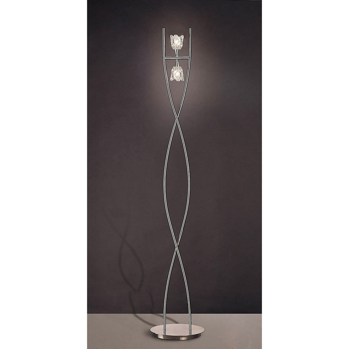 The Amel 2 Light Floor Lamp in polished chrome features a modern, twisting metal frame and two glass fixtures on a round base, shown against a dark background.