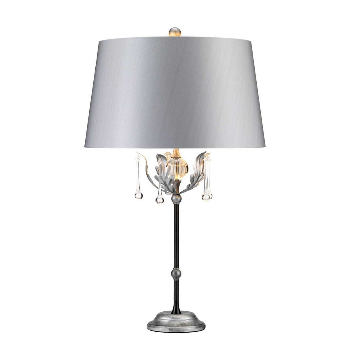 The Amarilli 1 Light Table Lamp - Black With Silver Patina is a decorative statement piece with a silver metal base and stem, featuring handcrafted detailing and crystal-like accents. It boasts a large gray drum lampshade and a small finial on top, enhancing its elegant appearance.