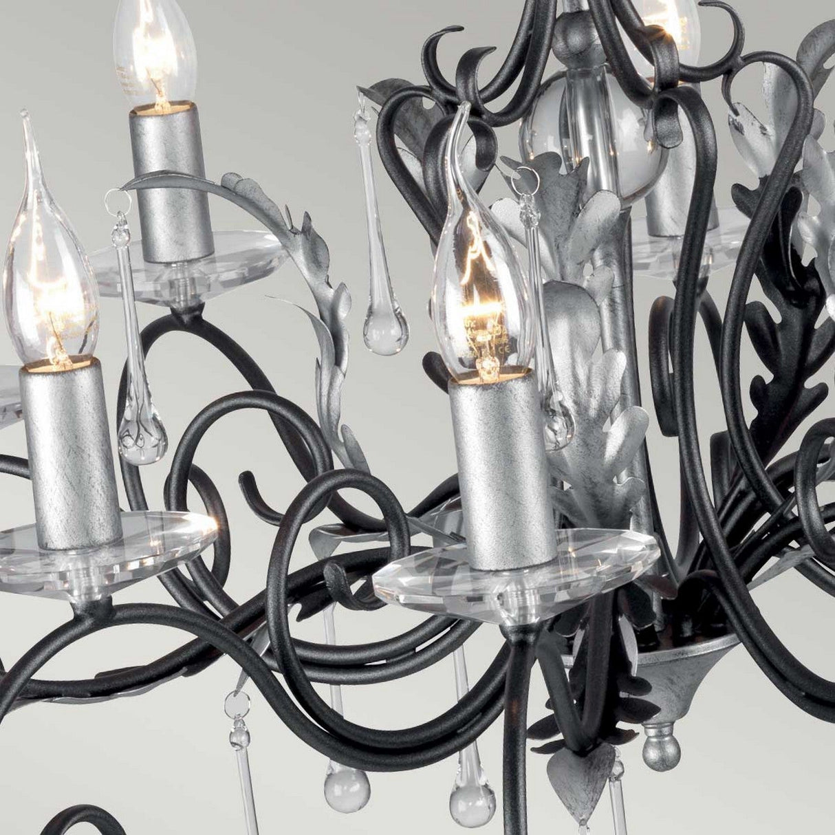 A detailed view of the Amarilli 10 Light Chandelier in Black with Silver Patina by Elstead Lighting highlights its five candle-shaped lights complemented by decorative metalwork and hanging crystal drops, all accentuated by the black with silver patina finish that enhances the chandelier's elegant and intricate design.