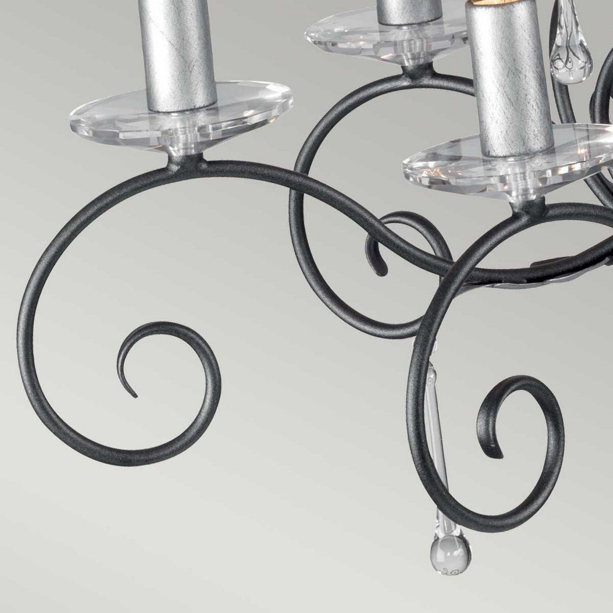 The Amarilli 10 Light Chandelier by Elstead Lighting showcases elegant swirling metal arms and candle-like light holders. The black with silver patina finish enhances its sophisticated look, while shimmering glass accents contrast beautifully against a soft, gradient light background.