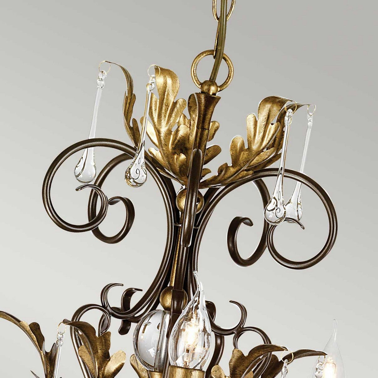 The Amarilli 15 Light Chandelier in bronze with gold patina is a decorative, handmade piece boasting intricate scrollwork and gold leaf accents. Its design features metal branches adorned with leaf shapes and numerous candle-shaped bulbs, all finished in a luxurious gold patina for an elegant and vintage aesthetic.