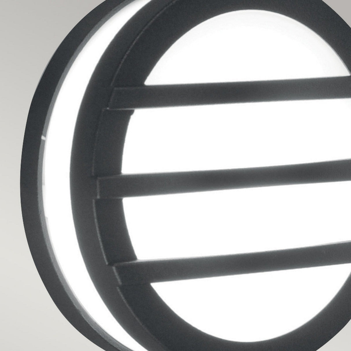 Close-up of the Ano-2 Outdoor Wall & Ceiling Light in Graphite, featuring a circular design with three horizontal black bars across its illuminated white surface. This minimalist fixture stands out against a neutral background and is ideal for energy-efficient outdoor lighting.