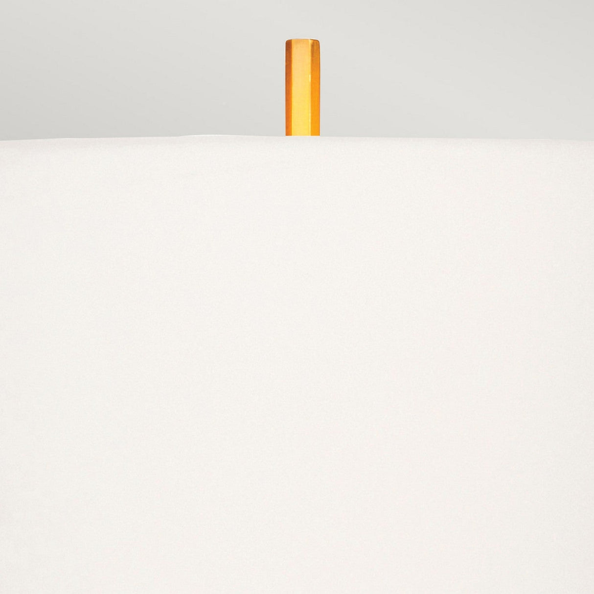 A minimalistic image features a white surface in the foreground, displaying a single vertical orange stick reminiscent of the Apollo Table Lamp With White Shade - Brushed Brass, protruding from the top center against a light gray background.