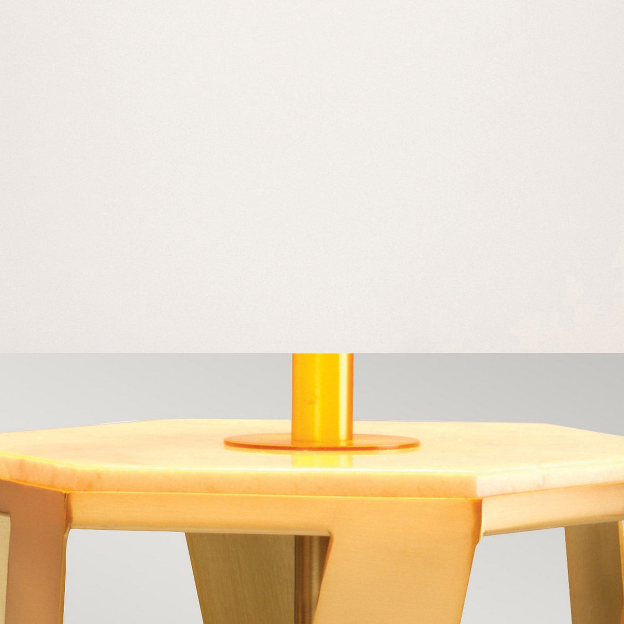 The Apollo Table Lamp With White Shade - Brushed Brass showcases a yellow cylindrical base resting on a wooden table, with its white shade offering a striking contrast. The neutral background highlights the simplicity and elegance of this design accentuated by brushed brass.