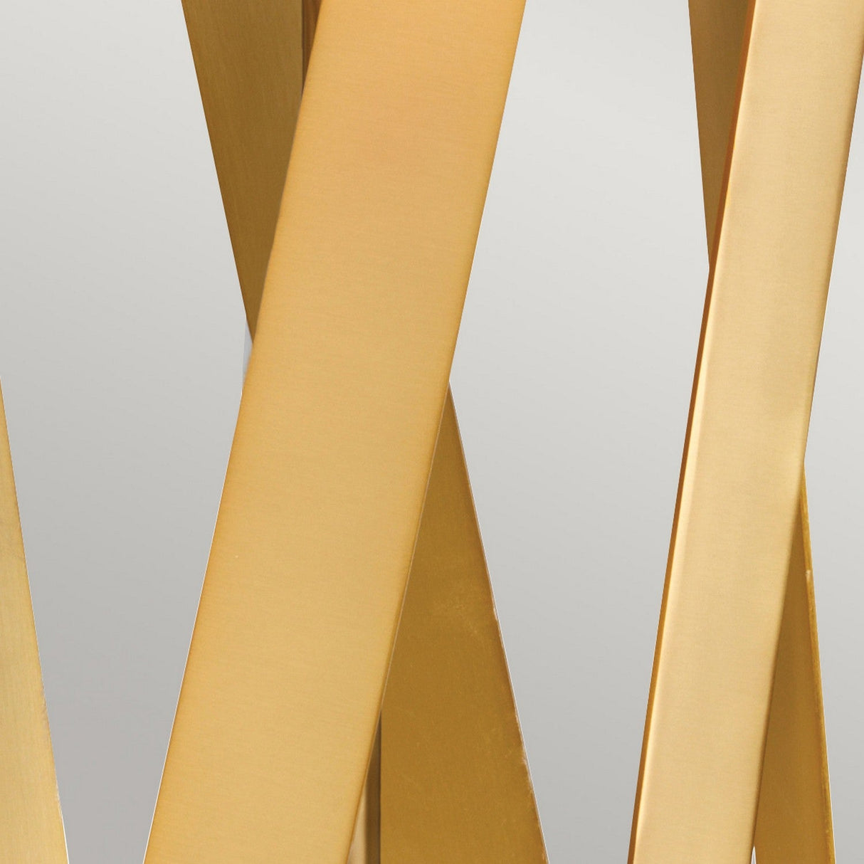 A close-up reveals abstract, overlapping beams of brushed brass set against a light gray background. Resembling the sleek lines of the Apollo Table Lamp With White Shade in Brushed Brass, these beams form a dynamic, crisscross pattern. The result is a modern and elegant appearance.