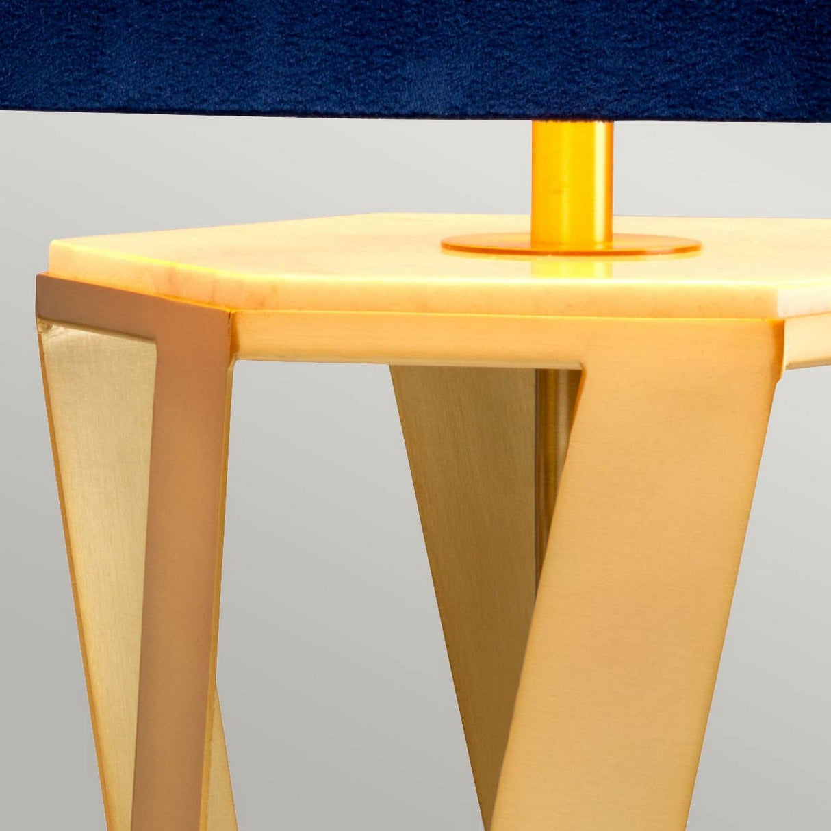 A close-up view of an Apollo Table Lamp showcases its modern design with a brushed brass base and a sleek geometric structure. The contrasting blue shade element perfectly complements the golden hexagonal top, creating a stylish and elegant appearance.