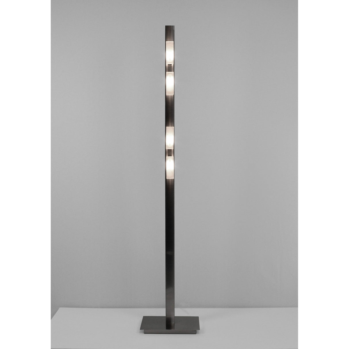 The Arco 4 Light Floor Lamp in satin nickel features a slim, modern design with three rectangular light panels evenly spaced on a square base, providing soft ambient lighting against a plain gray background.