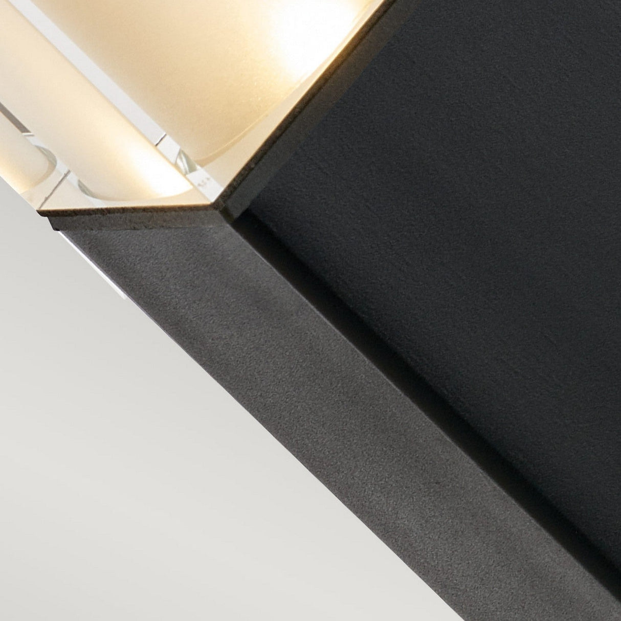 Close-up of the Arendal 1 Light Medium Bollard - Black, showcasing its modern geometric design ideal for coastal lighting. The fixture features a black matte texture complemented by clear and frosted glass panels, providing soft light diffusion. The image highlights a section of the structure against a neutral background.