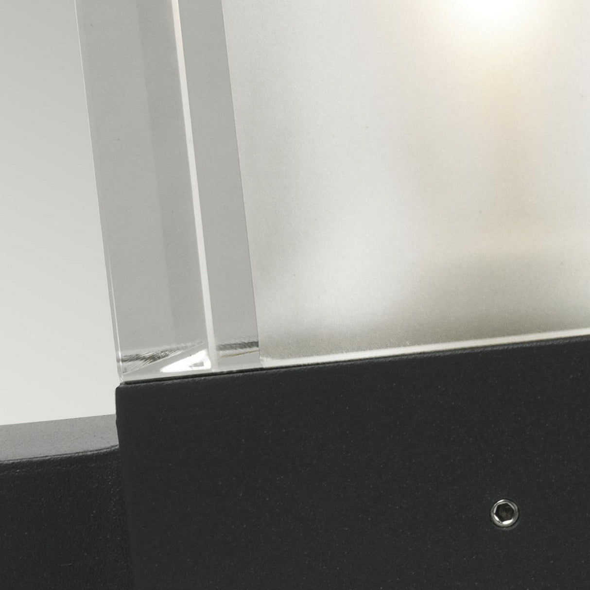 Close-up of the Arendal Outdoor 1 Light Wall Light in black, showcasing a frosted glass panel encased in a matte black metal frame with an IP65 rating. The visible screw detail complements its black powder-coated finish, while the soft glow illuminates part of the glass.