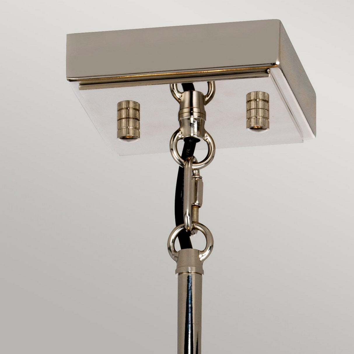 Shown in the image is the Aries 4 Light Small Chandelier in polished nickel, featuring a rectangular base with two screw fittings. It elegantly suspends from a black cable and a metallic rod, connected by a circular ring, set against a plain light-colored backdrop.
